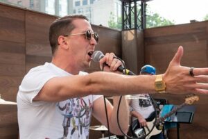 Walker Dieckmann (tall white male with dark hair in a light blue t-shirt) of the Roland High Life sings his heart out at the Emerson College Uncommon Stage in Boston, Massachusetts